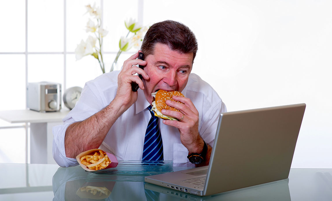 Man eating a hamburger and fries in front of a laptop